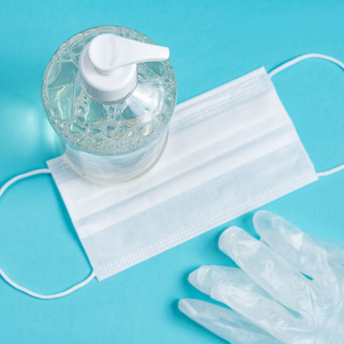 Container with alcohol gel, gloves and surgical mask on the ligh